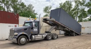 Shipping container delivery by truck on a flatbed trailer, being ground-delivered on-site.