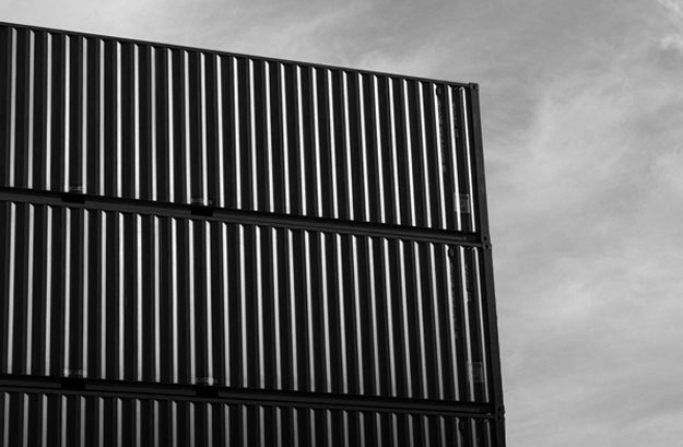 Photo artistique en noir et blanc mettant en valeur les formes et les lignes de conteneurs maritimes empilés.