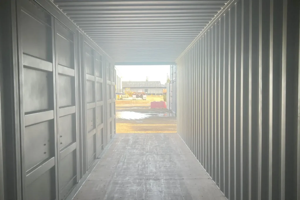 Interior view looking out of an open 40ft High Cube side-opening shipping container toward a bright industrial worksite.