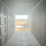 Interior view looking out of an open 40ft High Cube side-opening shipping container toward a bright industrial worksite.