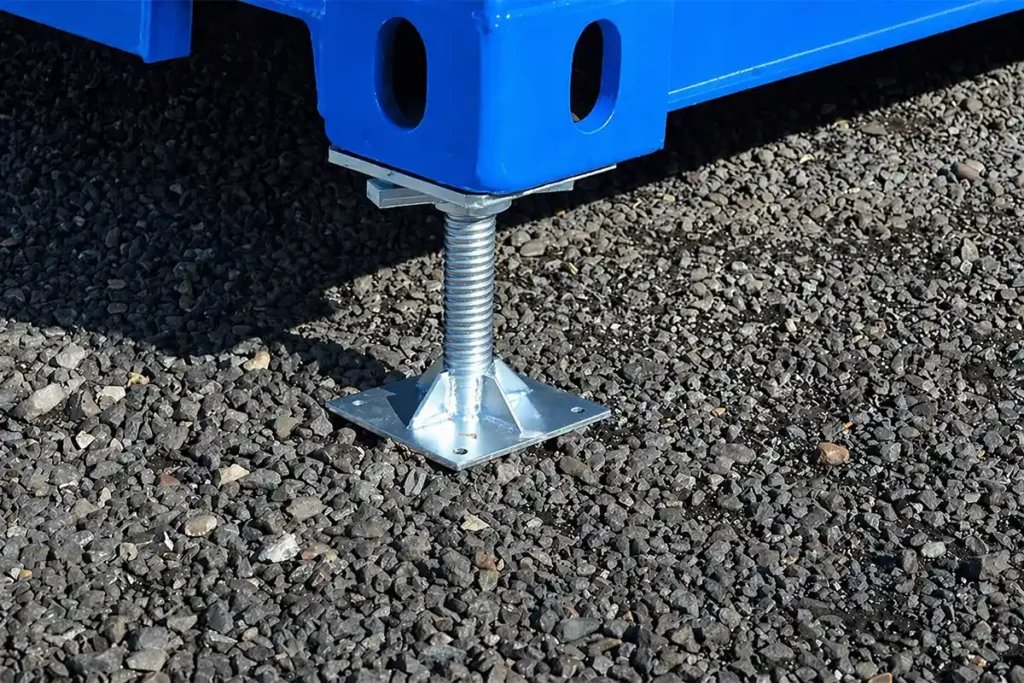 Adjustable steel leveling leg stabilizing a blue shipping container on a gravel job site