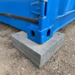 Close-up of the steel corner casting of a commercial shipping container resting securely on a stackable leveling pad.