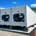 Multiple black shipping container levelling pads stacked to support the bottom corner of a sea can on uneven ground.